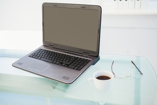 Laptop na mesa com uma caneca de café e óculos