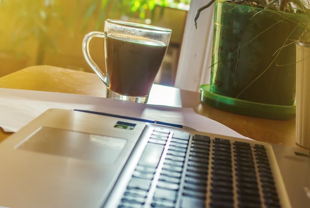 Laptop nah oben von einer Tastatur und von einer Schale heißem Kaffee morgens. Selektiver Fokus