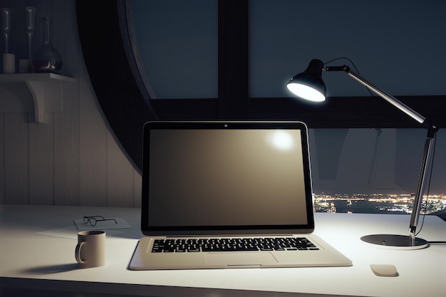 Laptop negra en blanco con taza de café y lámpara por la noche