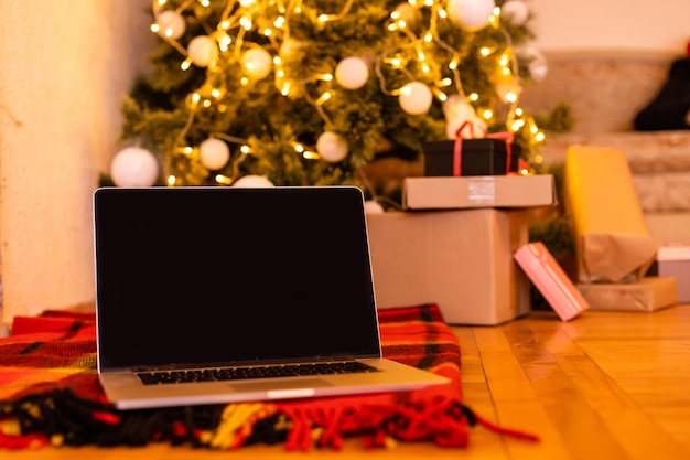 Laptop no fundo de uma árvore de Natal aceita parabéns on-line, feliz Natal. Videochamada com a família em tempos de coronavírus.