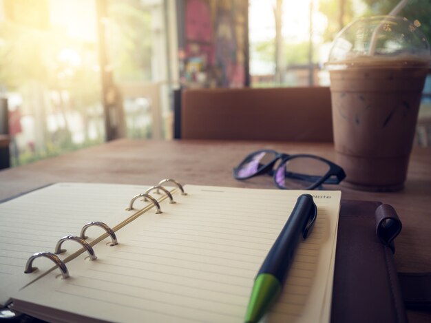 Laptop (notebook) com copo de café gelado e o bloco de notas com a caneta na mesa de madeira velha.