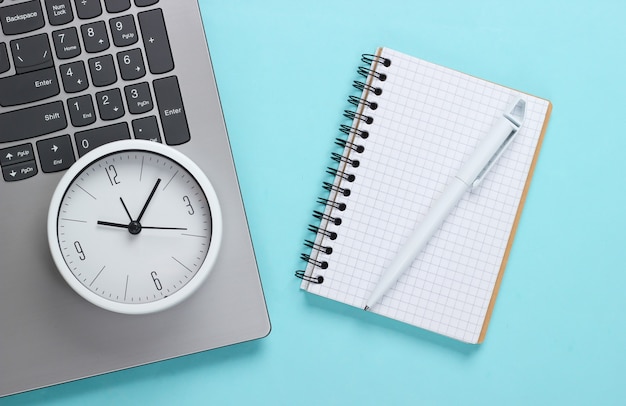 Laptop, notebook e despertador sobre fundo azul. O tempo está fugindo. O conceito de prazos urgentes no trabalho e compromissos.