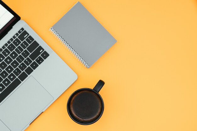 Laptop, notebook e xícara com café em uma superfície laranja, vista superior, local de trabalho