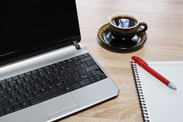 Laptop, Notizbuch aus Papier mit Stift und Tasse Kaffee auf der Tischnahaufnahme