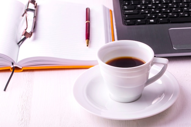 Laptop, Notizbuch mit einer Tasse Kaffee und einem Bleistift auf einem Holztisch liegend