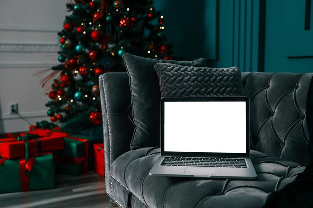 Laptop con pantalla en blanco en un escritorio y árbol de Navidad con luces en el fondo