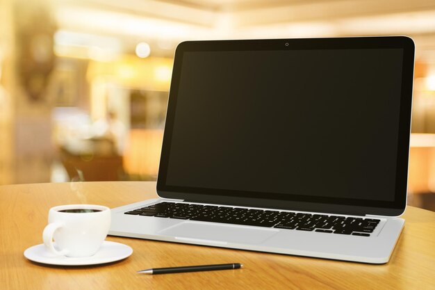 Laptop con pantalla en blanco en una mesa de madera con taza de café y bolígrafo