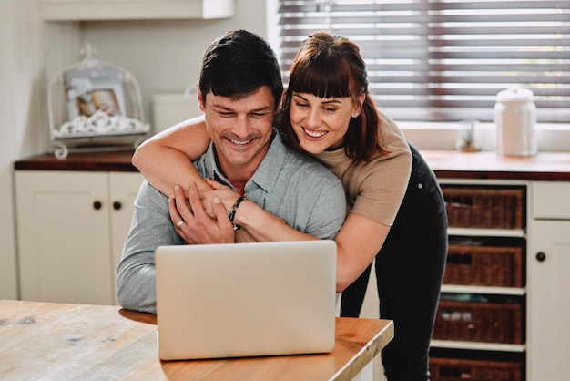 Laptop pareja y abrazo en la cocina lectura y sonrisa para el correo electrónico de trabajo remoto en línea y empleo personas mujer y hombre con computadora abrazo y amor para felicitaciones de contratación en el trabajo y el hogar