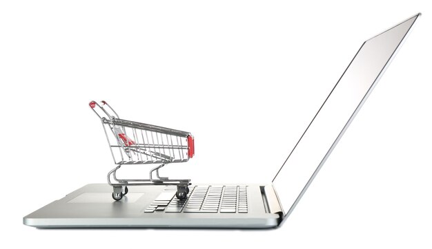 Laptop con un pequeño carrito de compras aislado sobre un fondo blanco