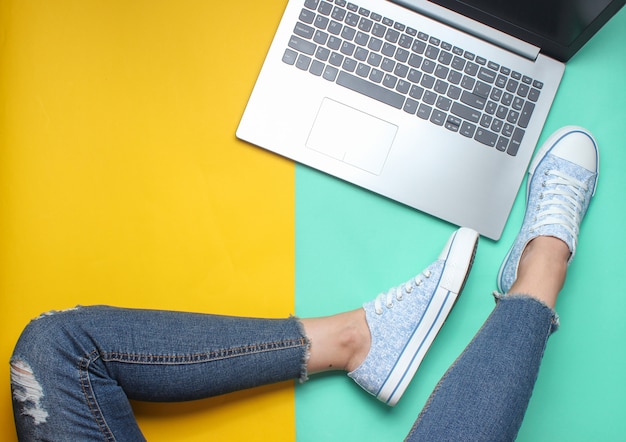 Laptop, piernas femeninas en jeans y zapatillas de deporte, estilo plano