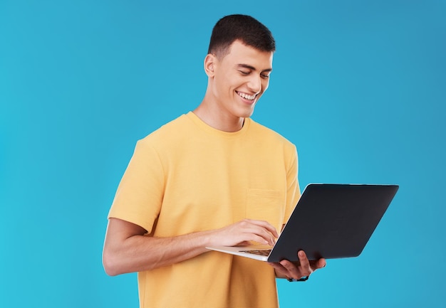 Laptop-Recherche und männlicher Student in einem Studio, der an einem Universitätsprojekt im Internet arbeitet Lächelnde Technologie und junge männliche Person, die für einen College-Test oder eine Prüfung am Computer vor blauem Hintergrund studiert