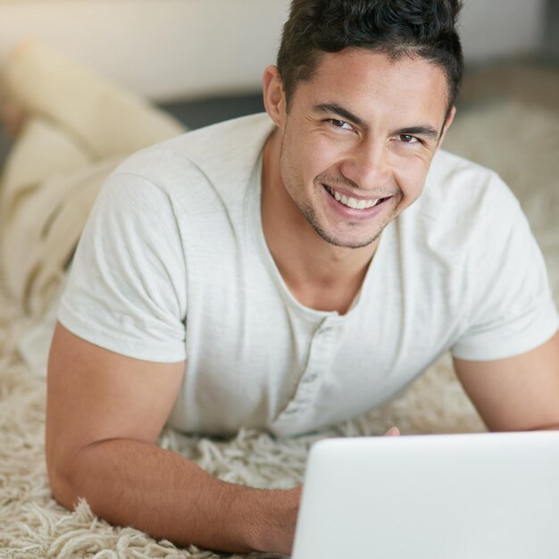 Laptop relajada y retrato de un hombre escribiendo en el piso de su casa o apartamento con una sonrisa tirada en una alfombra de comercio electrónico feliz y joven hombre o trabajador independiente haciendo trabajo o proyecto remoto