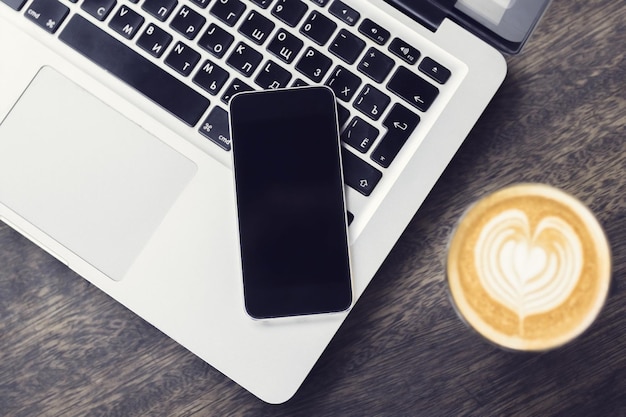 Laptop, smartphone e cappuccino numa mesa de madeira