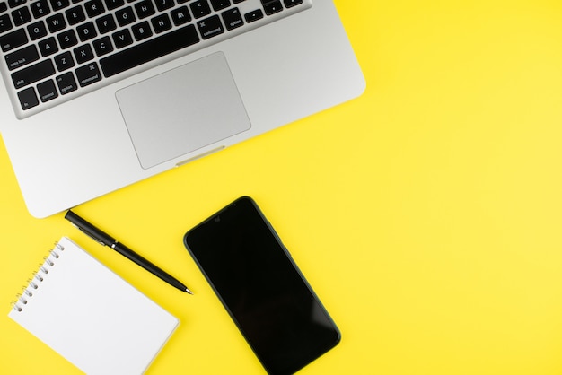 Laptop, Stift, Notizblockplaner und Smartphone auf gelbem Hintergrund.