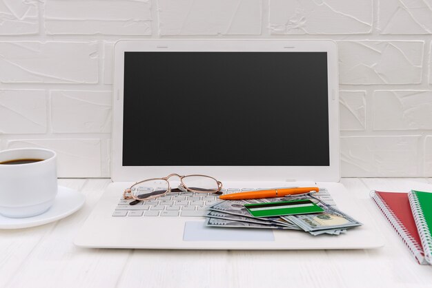 Laptop, tarjeta de crédito, dólares y taza de café.