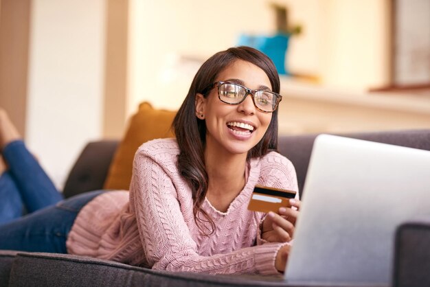 Laptop de tarjeta de crédito y mujer en el sofá en casa con felicidad por pagar facturas con estilo de vida sin deudas sonrisa computadora y persona femenina con aplicación de banca por Internet para solicitar una hipoteca en el apartamento