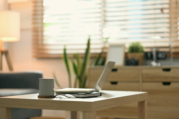 Laptop Tasse Kaffee und Bücher auf Holztisch im gemütlichen Wohnzimmer