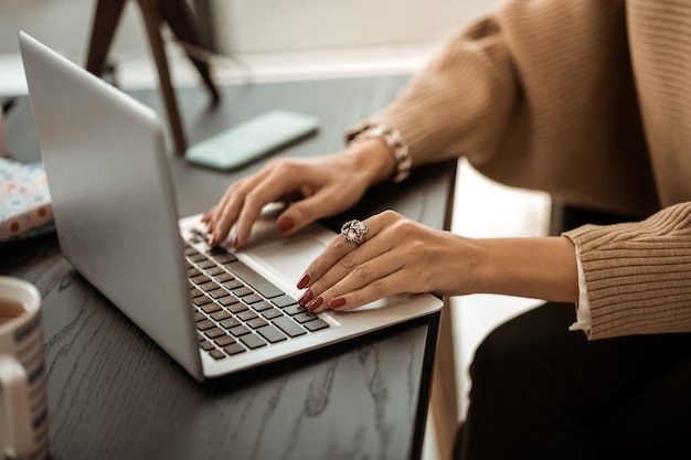 Laptop-Tastatur. Ordentliche Frau im beigen Pullover mit roter Maniküre und Seltenheitsring am Zeigefinger