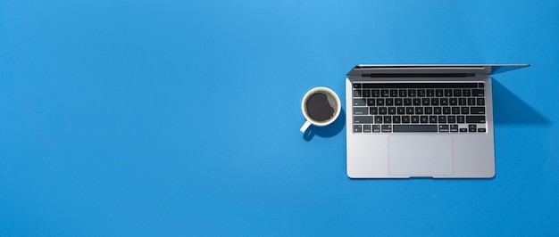 Laptop y taza de café sobre fondo azul.