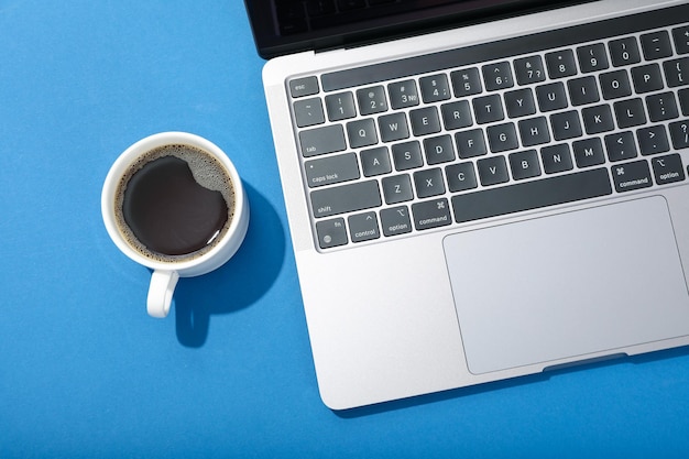 Laptop y taza de café sobre fondo azul.