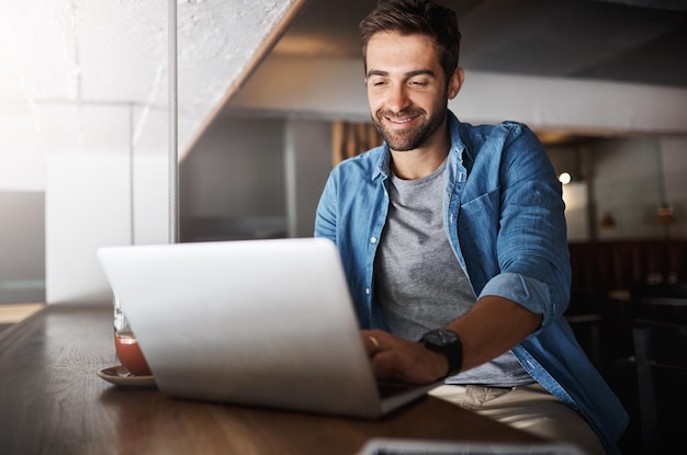 Laptop trabajo remoto y sonrisa con el hombre en el café para la creación de redes o la planificación en línea Información informática y lectura con feliz empleado independiente en la cafetería como cliente para la hospitalidad o el servicio
