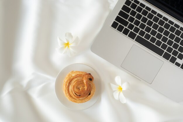 Laptop und Brot und Blumen auf weißem Stoffhintergrund das Konzept des Online-Lernens