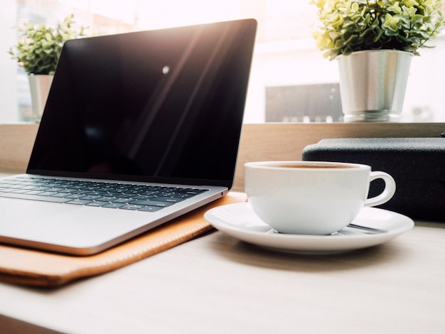 Laptop und eine Tasse Kaffee mit Morgenlicht im Café.