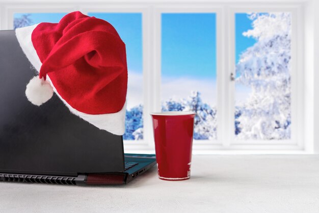 Laptop und Geschenke auf dem Tisch mit Santa Claus-Hut zu Hause mit einem Panoramablick