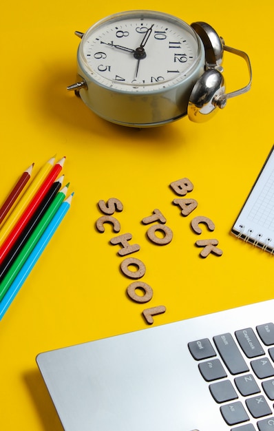 Laptop und Notizbuch mit Buntstiften in der Nähe einer Uhr