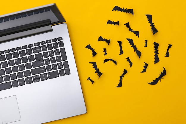 Laptop und Scherenschnitt Fledermäuse auf gelbem Grund. Halloween-Thema. Ansicht von oben