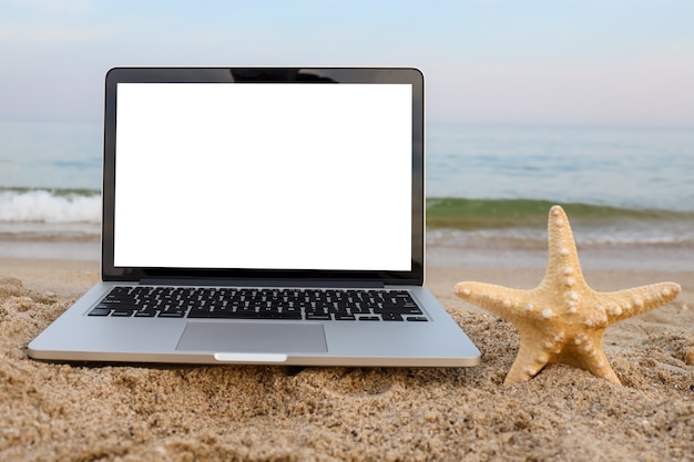 Laptop und Seesterne auf dem Sand am Strand im Sommer im Hintergrund mit weißem Bildschirm.