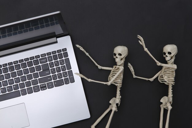 Laptop und Skelette auf schwarzem Hintergrund. Halloween-Thema. Ansicht von oben