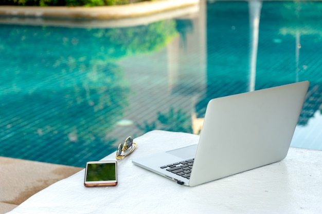 Laptop und Smartphone nahe dem Swimmingpool, moderner Geschäftsmann können überall arbeiten.