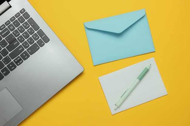 Laptop und Umschlag mit Brief auf gelbem Hintergrund. Valentinstag. Draufsicht