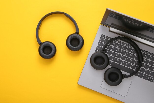 Laptop und zwei Paar schwarze drahtlose Stereokopfhörer auf gelbem Hintergrund