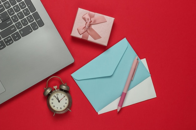 Laptop, Wecker, Santa Briefumschlag, Geschenkboxen mit Schleife auf rotem Hintergrund. 11:55 Uhr. Neujahr, Weihnachtskonzept. Draufsicht