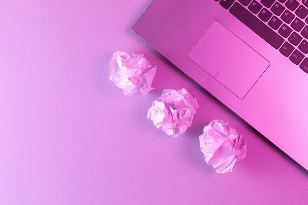 Laptop, zerknitterte Papierkugeln schließen. Holographisches rosa Licht