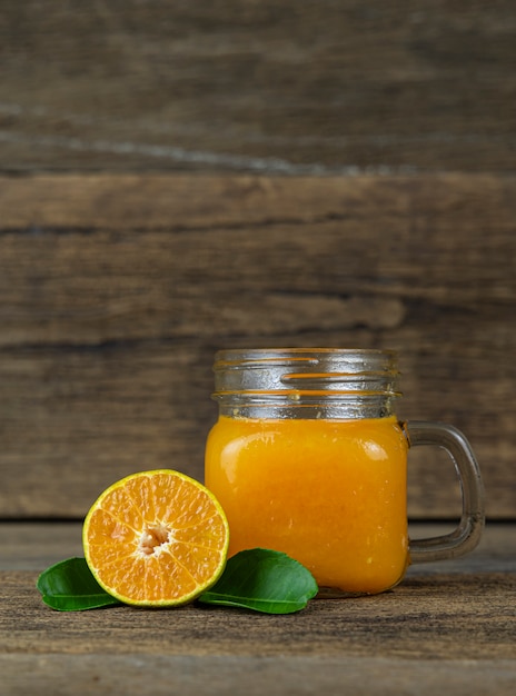 Foto laranja cortada ao meio e um copo de suco de laranja na parede da mesa de madeira.