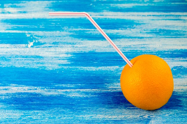 Foto laranja madura com tubo para cocktail no fundo azul