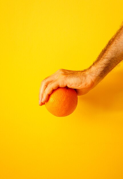 Laranja na mão na parede amarela ii
