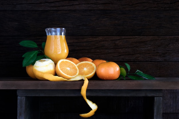 laranjas frescas com folha e suco de laranja em vidro na mesa de madeira