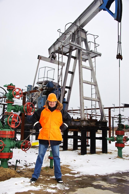 Ölarbeiter in orangefarbener Uniform und Helm auf dem Hintergrund der Pumpenbuchse.