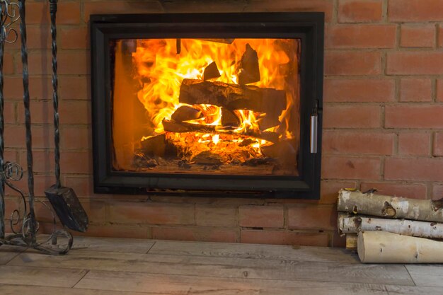 Lareira com fogo ardente no interior de uma casa de madeira Lenha e um conjunto de lareira estão localizados perto da lareira com chama