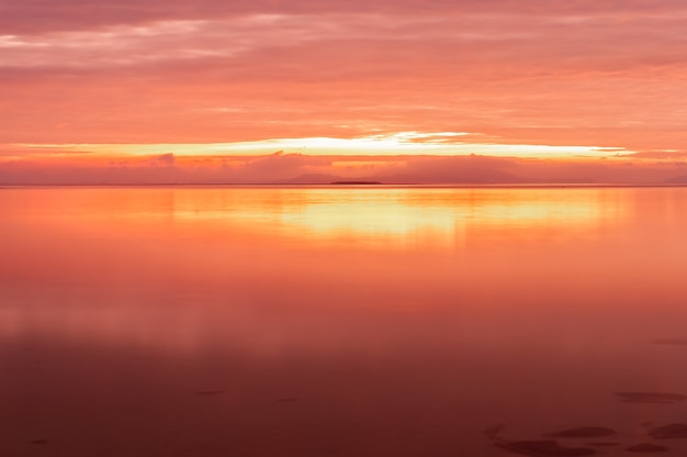 La larga exposición de un amanecer radiante con un color rosa amarillo reflejado en la suave superficie del océano en la playa de Nakano, isla Iriomote