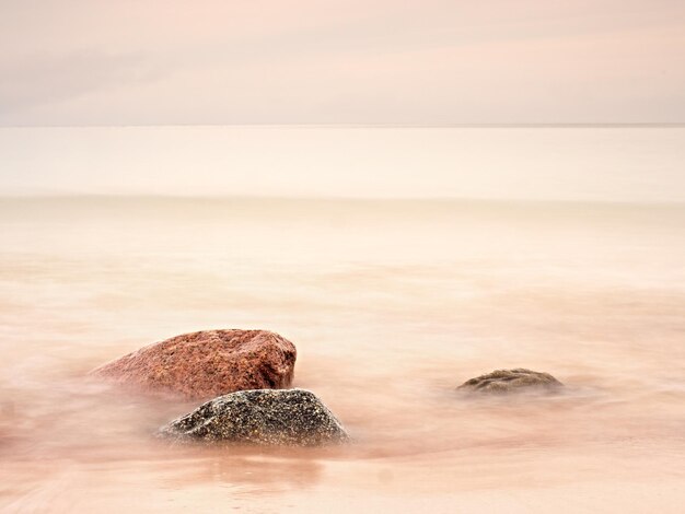 Foto larga exposición del mar y grandes rocas que sobresalen el atardecer rosado en la costa rocosa del mar de balsitc