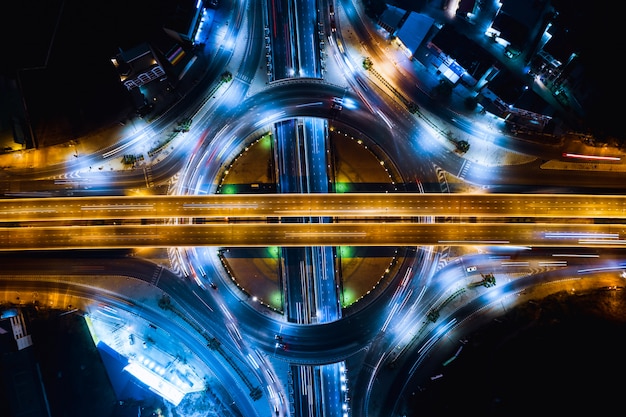 Foto larga exposición en el tráfico nocturno del semáforo en la carretera de circunvalación y las autopistas sobrepasan la intersección que conecta el negocio de logística de transporte de la ciudad en tailandia