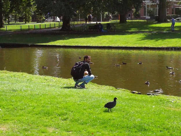 El largo de un hombre agachado por un canal en el parque