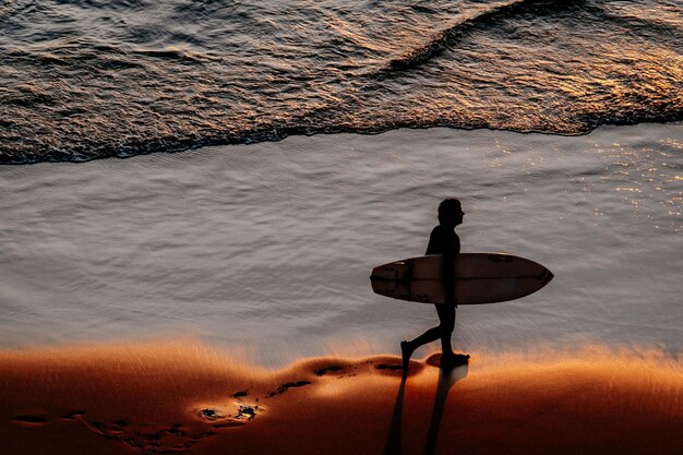 El largo de un hombre caminando por la playa durante la puesta de sol