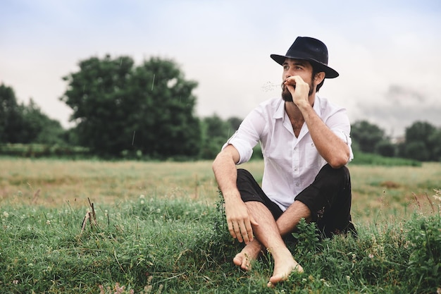 Foto el largo de un joven pensativo que mira hacia otro lado mientras está sentado en un campo de hierba