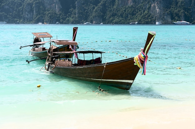Foto largos botes se paran en la isla de phi phi. se puede ver agua azul clara.